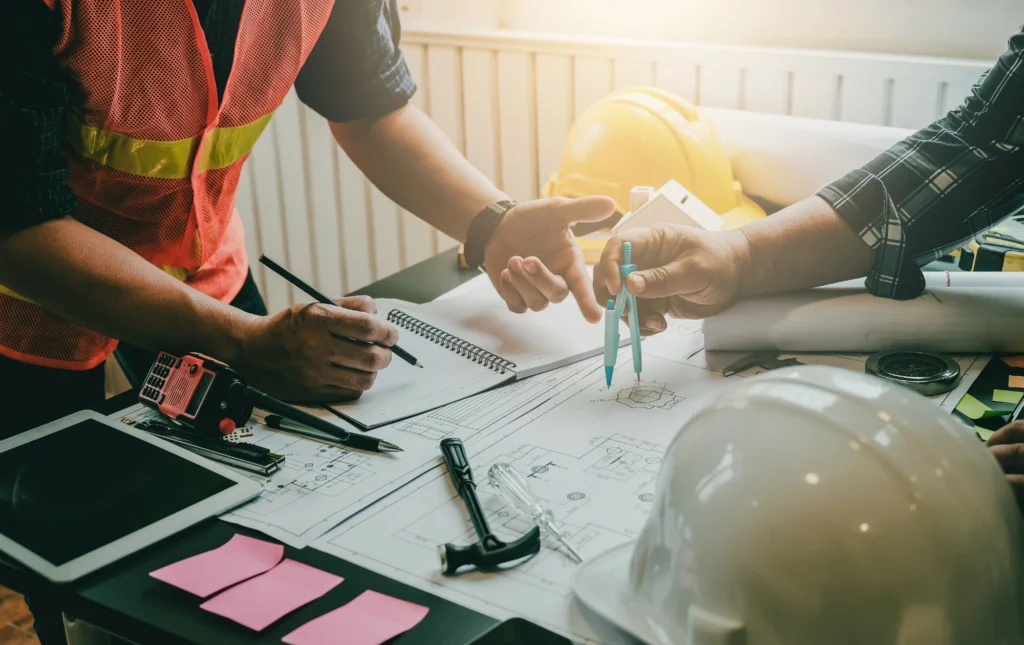 Équipe de chantier en réunion de planification devant un tableau blanc avec planning visible.